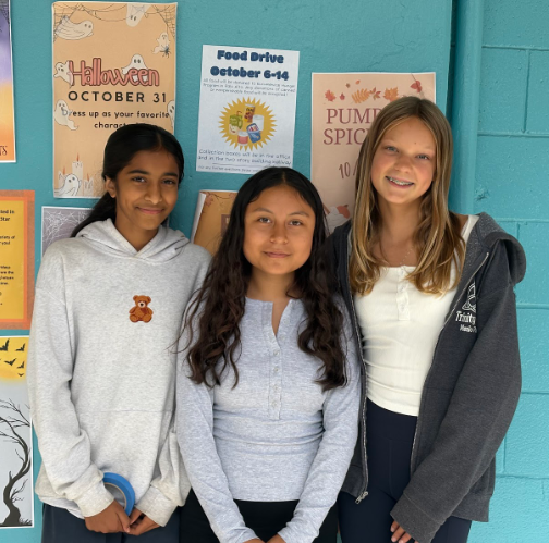 8th graders Sudha S, Susana S, and Kiersten M pose by their poster for a food drive they organized for their 8th grade Capstone Project.